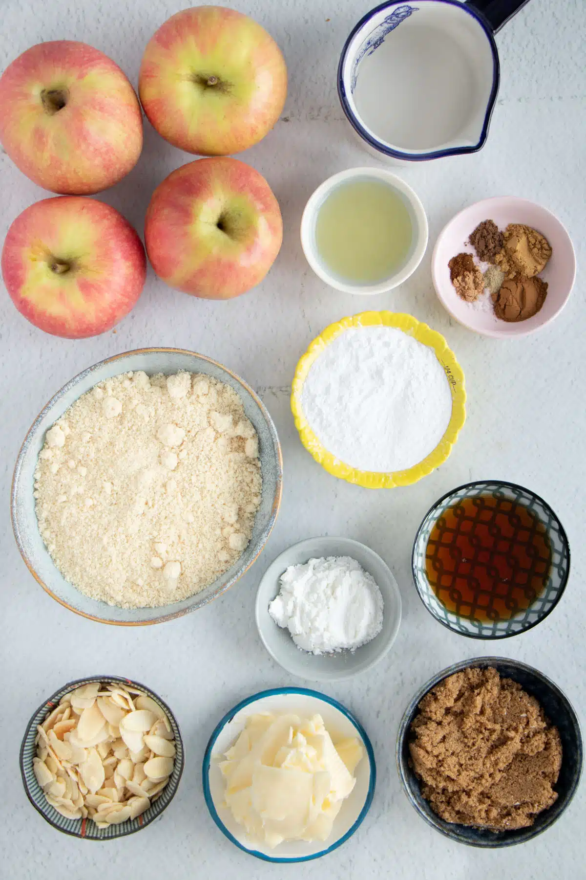 All the ingredients needed to make an apple crisp without oats are spread out across a table in bowls.