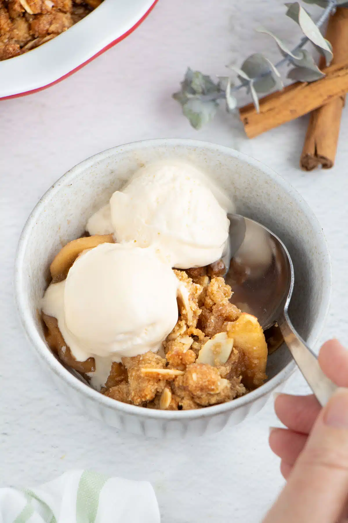A small bowl of gluten free apple crisp has been served with vanilla ice cream on top.