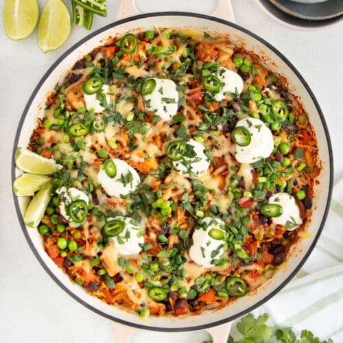 A large French sauté pan is filled with Cheesy Mexican Chicken And Rice topped with sour cream and herbs.