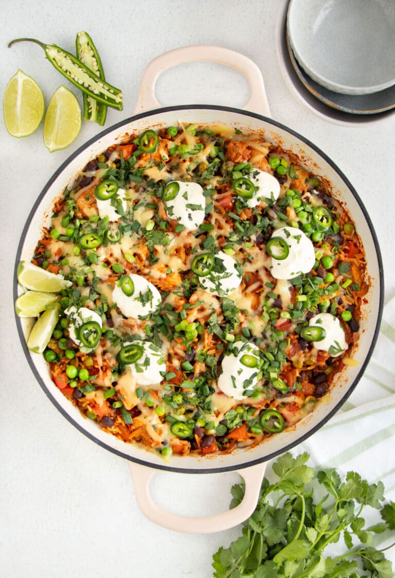 A large French sauté pan is filled with Cheesy Mexican Chicken And Rice topped with sour cream and herbs.
