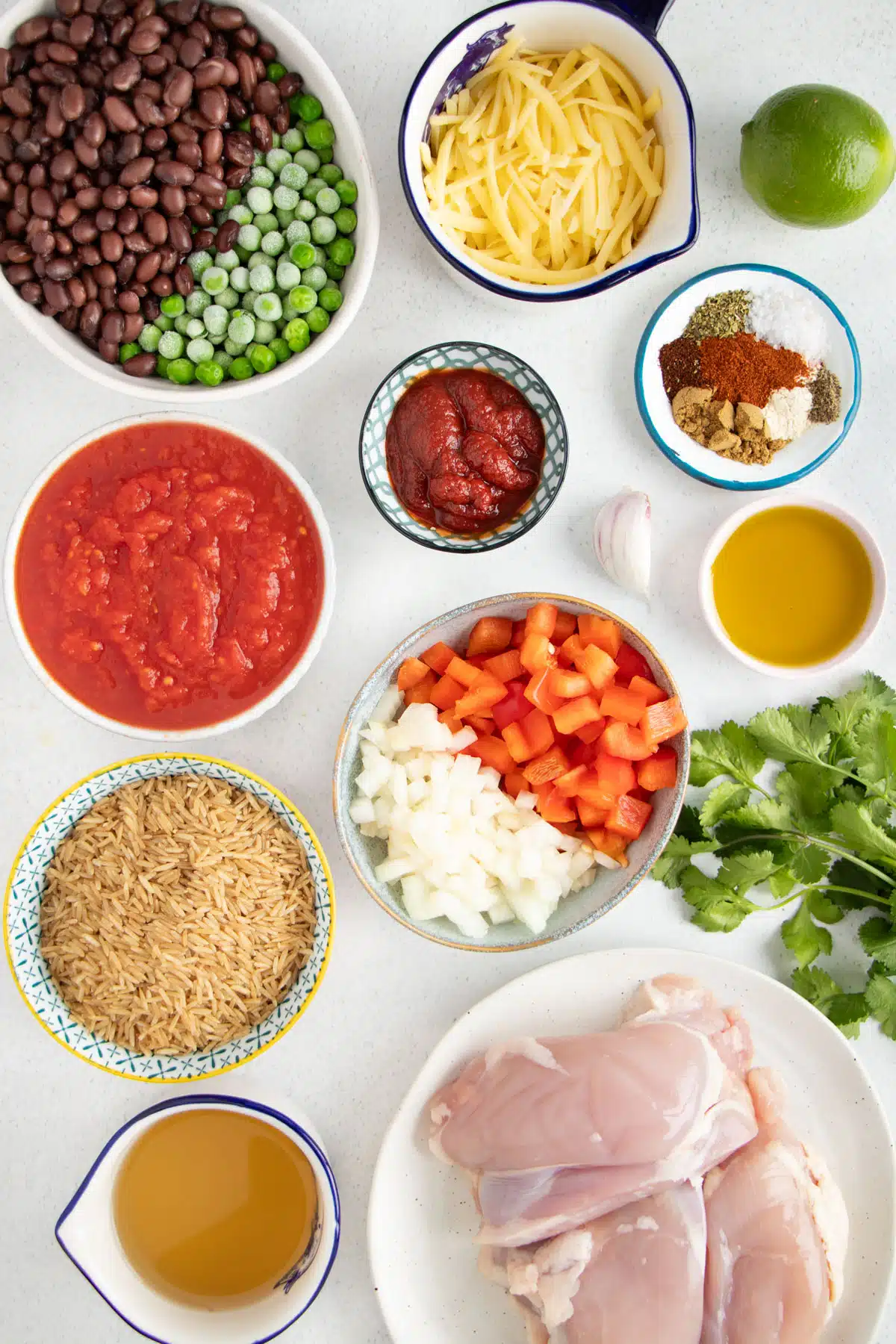 All the ingredients needed to make Cheesy Mexican Chicken And Rice are laid out across a table in bowls.