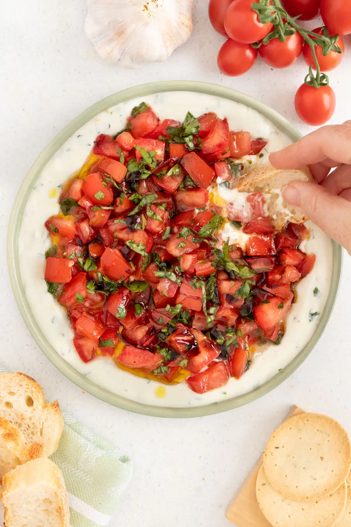 A white hand is dipping a slice of baguette into a Bruschetta Dip.
