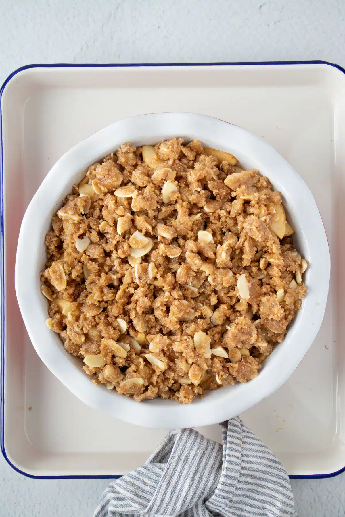 A fully assembled apple crisp without oats in a pie dish ready for the oven.