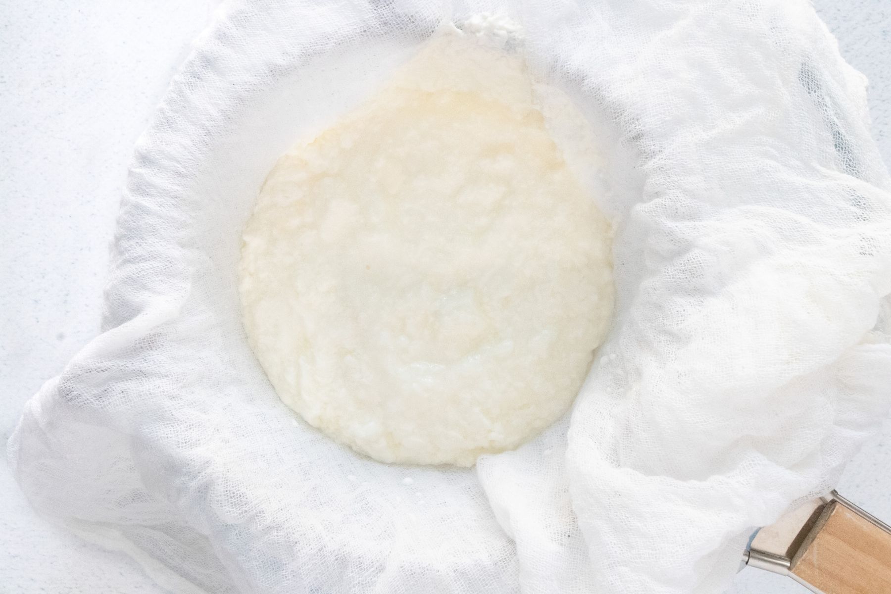 Yoghurt has been poured into a strainer lined with white cheesecloth.