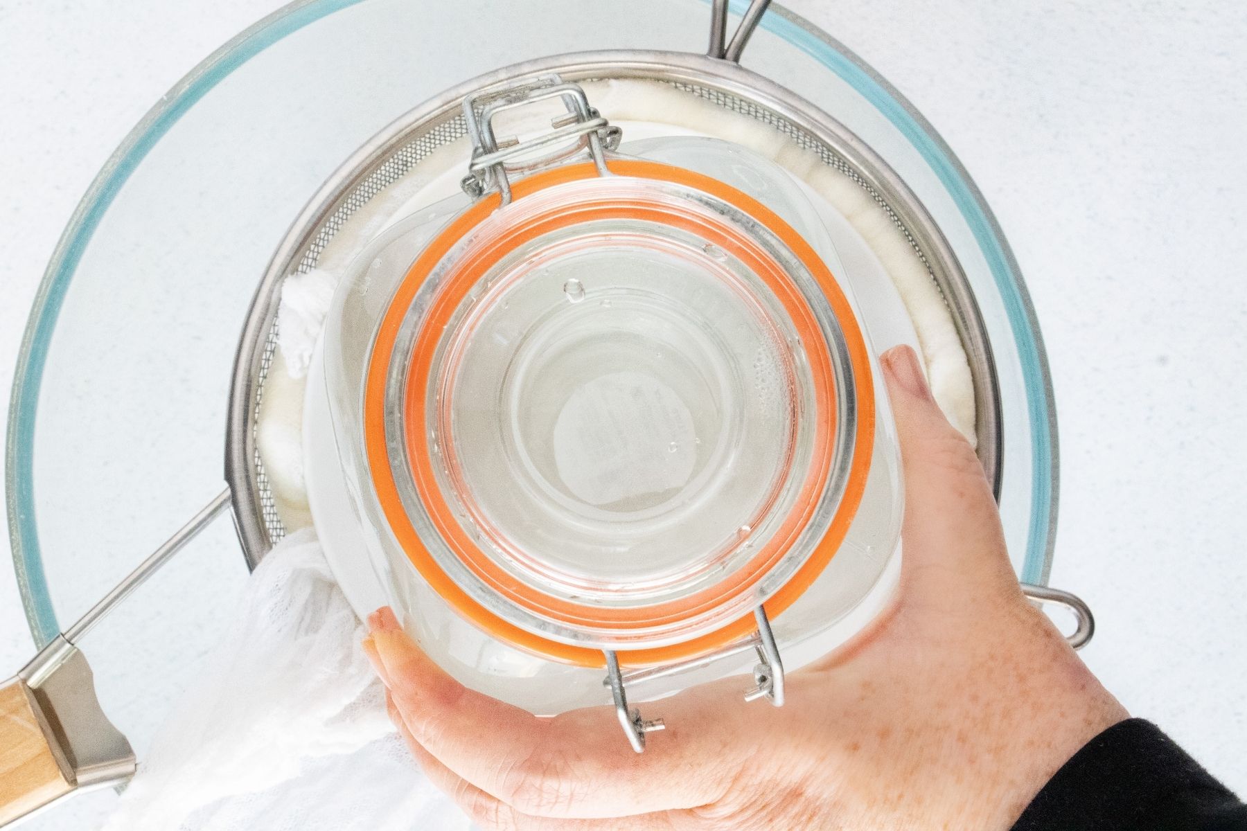 A large jar filled with water sits on a saucer atop the straining yoghurt to help weigh it down.