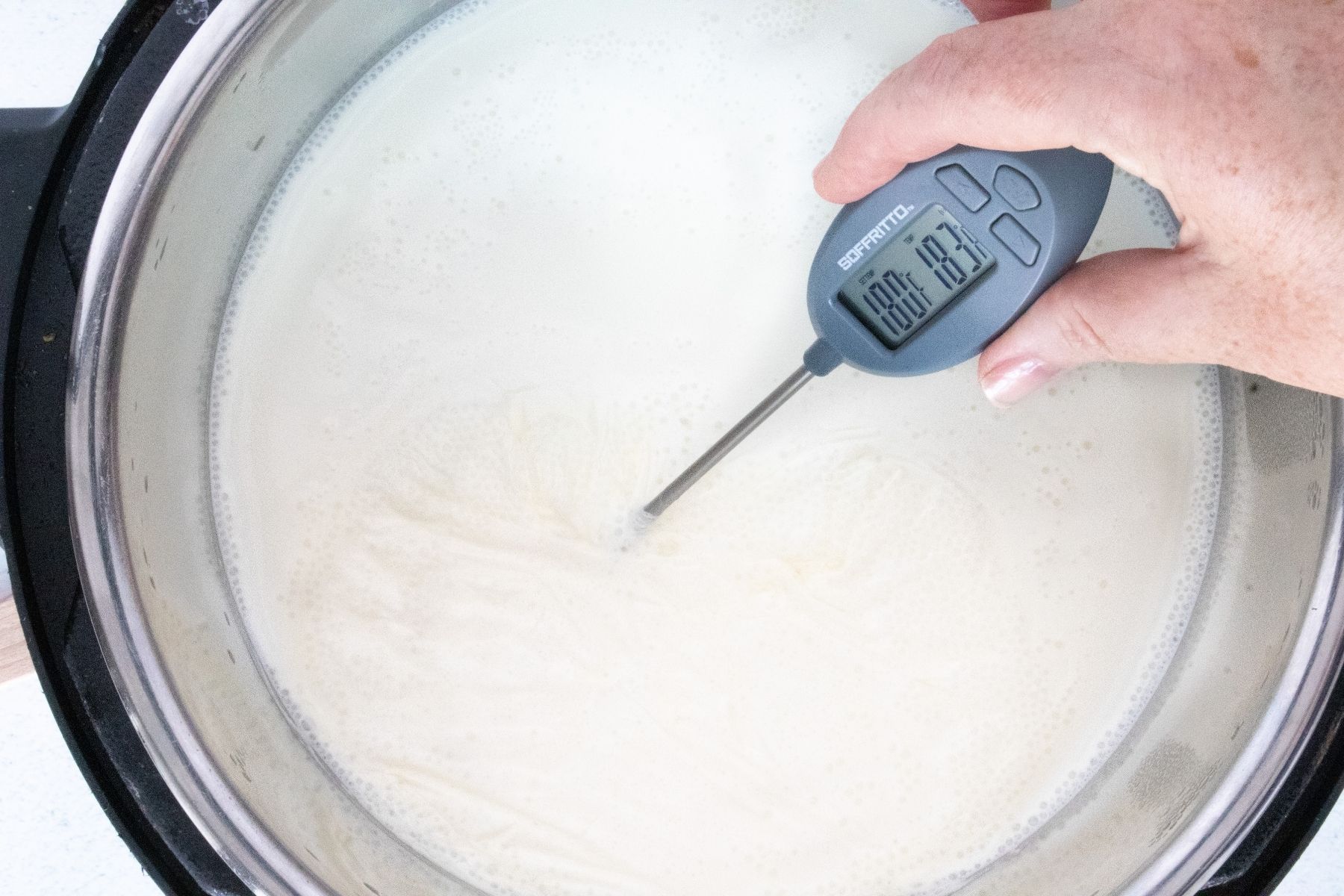 A white hand has a digital thermometer sitting in the just-boiled milk. It reads 183ºF.