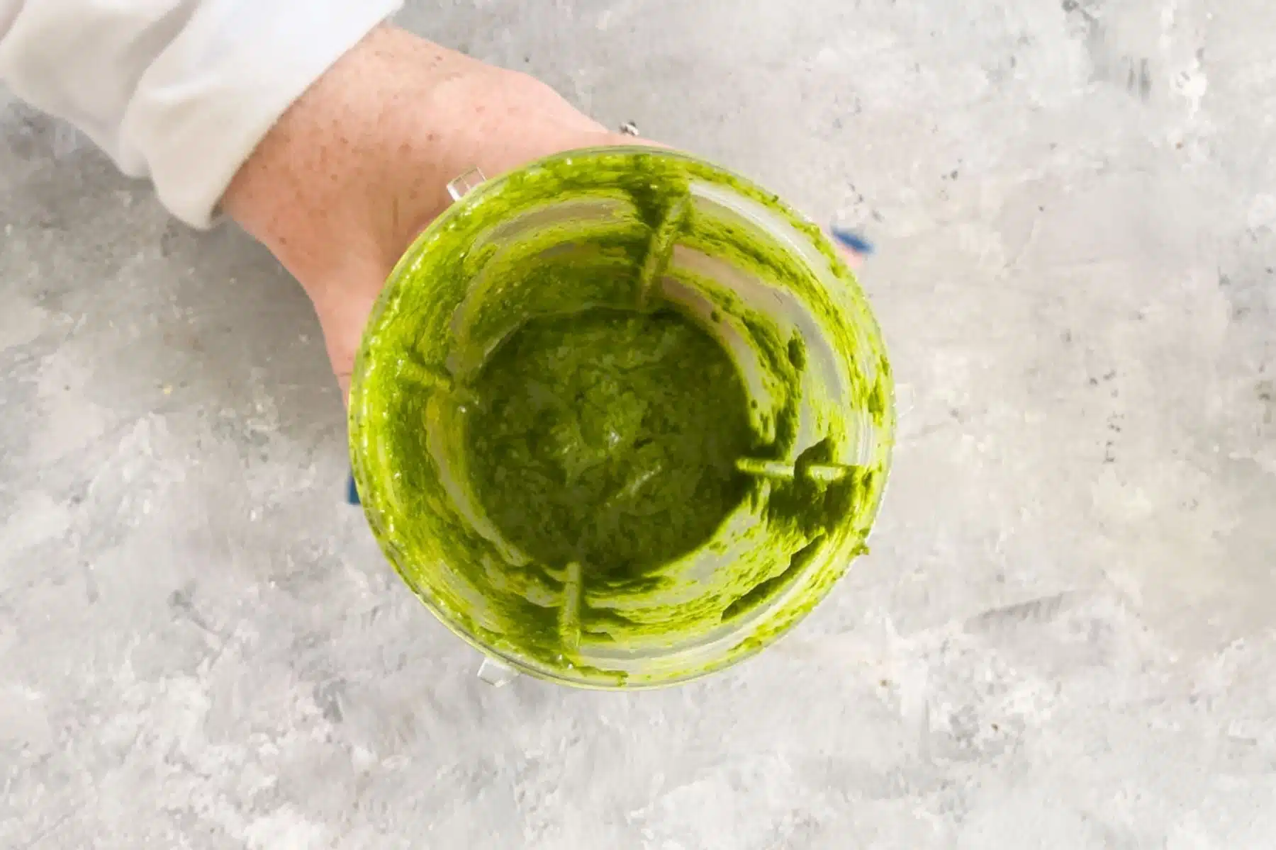 A white hand is holding a nutribullet blender cup filled with bright green pesto.