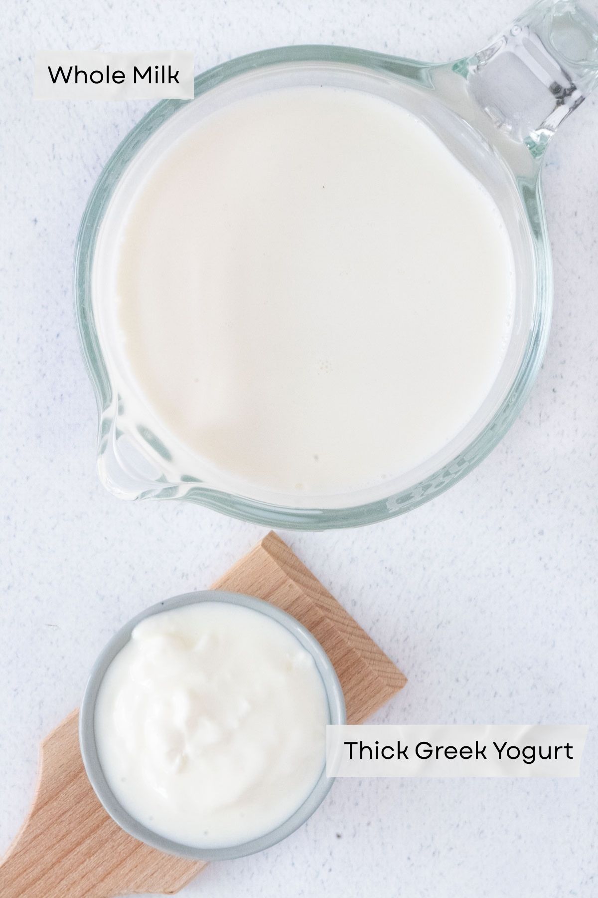 A jug of milk and a small bowl of yogurt are sitting on a white tabletop. The two ingredients to make Instant Pot Greek Yogurt.