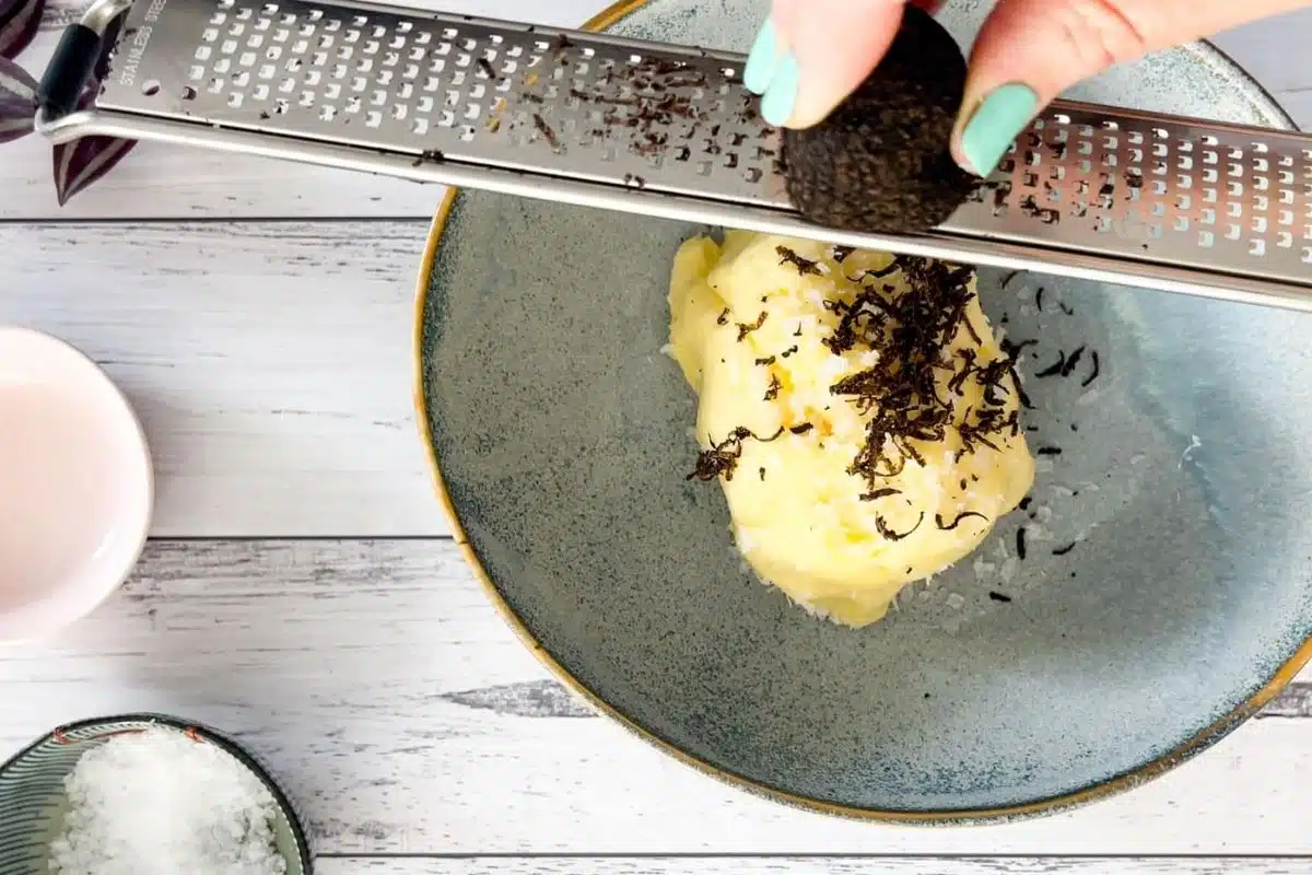 Black truffle is being grated over bright yellow butter with a microplane.