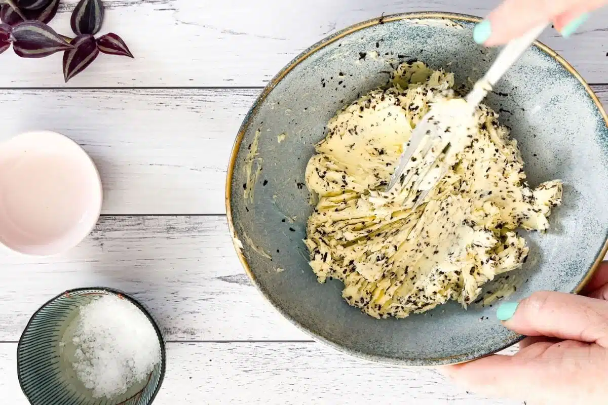 Truffle butter is being mixed together in a blue bowl with a fork.