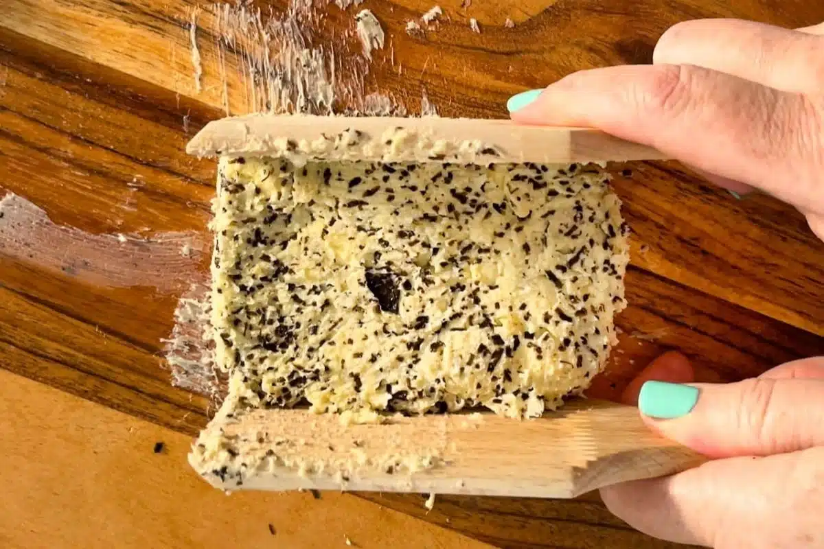 Two white hands are holding butter paddles that are being used to shape truffle butter into a block.