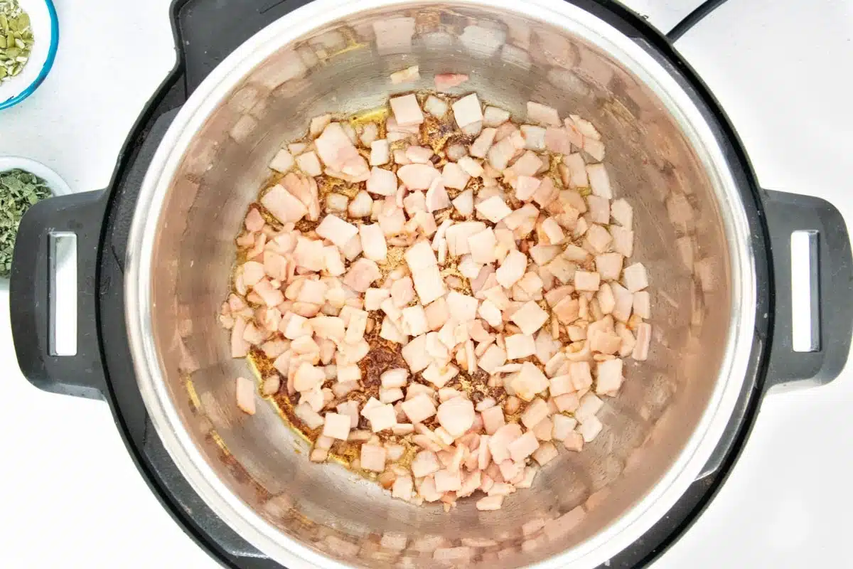Chopped bacon is sautéing and browning in the bottom of an instant pot.