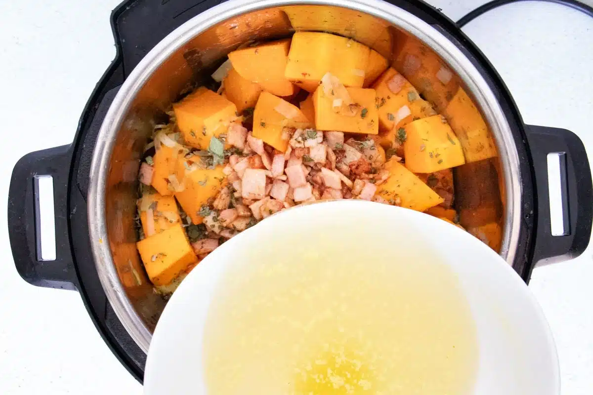 Chicken stock is being added to an instant pot full of chopped pumpkin, bacon and herbs.