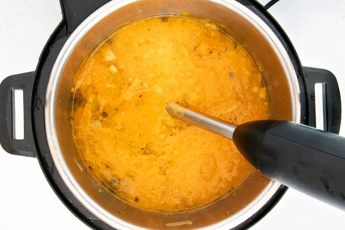 Bright orange butternut squash soup being blended with an immersion blender.