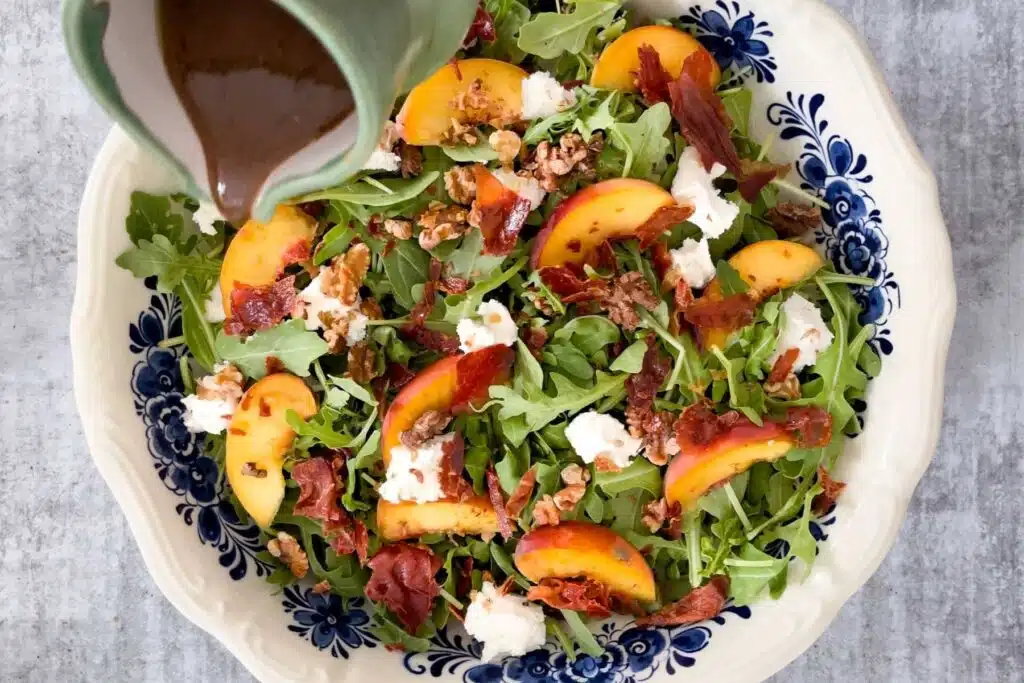 A balsamic vinaigrette is being poured from a small green jug over the assembled salad.