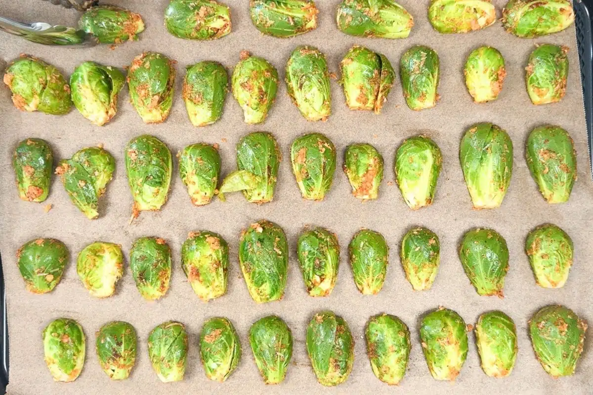 Placing garlic parmesan brussels sprouts face down on a parchment-lined baking tray.