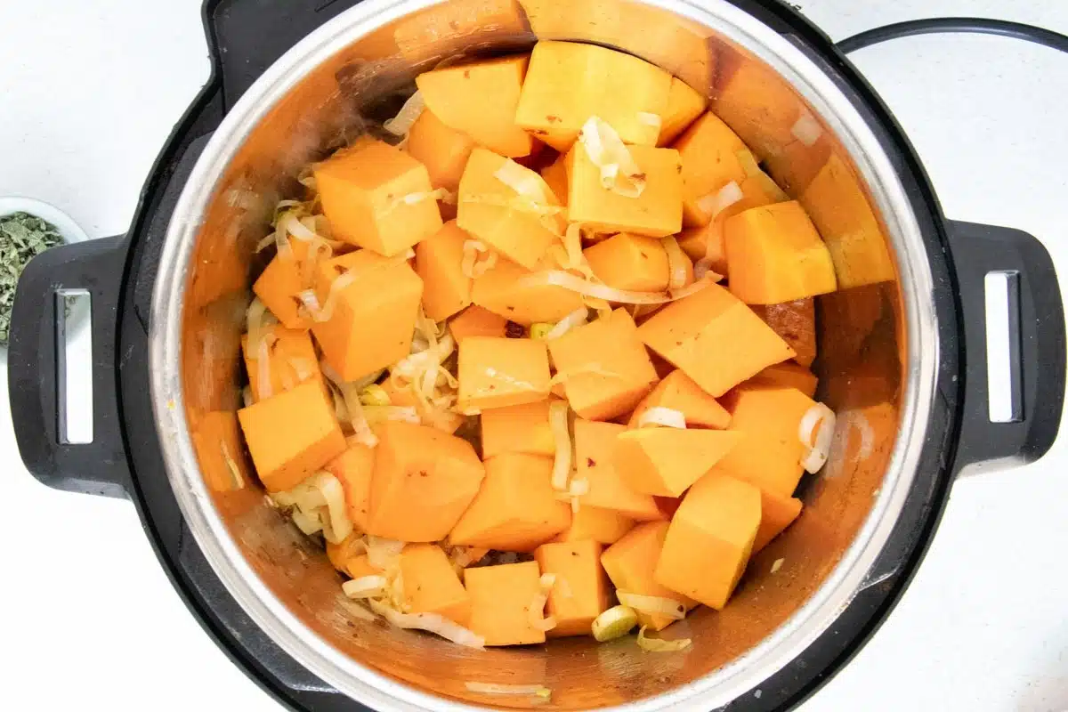Looking down into the silver bowl of an instant pot to see chopped butternut squash and leek.