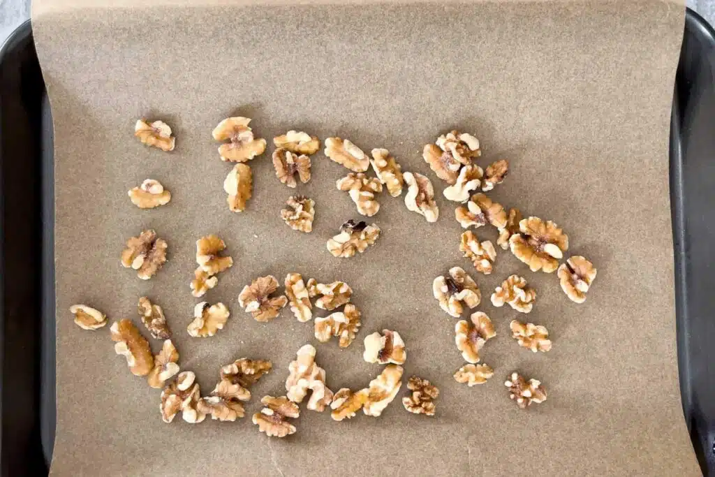A small baking tray lined with baking paper has walnuts spread across ready to go in the oven for toasting.