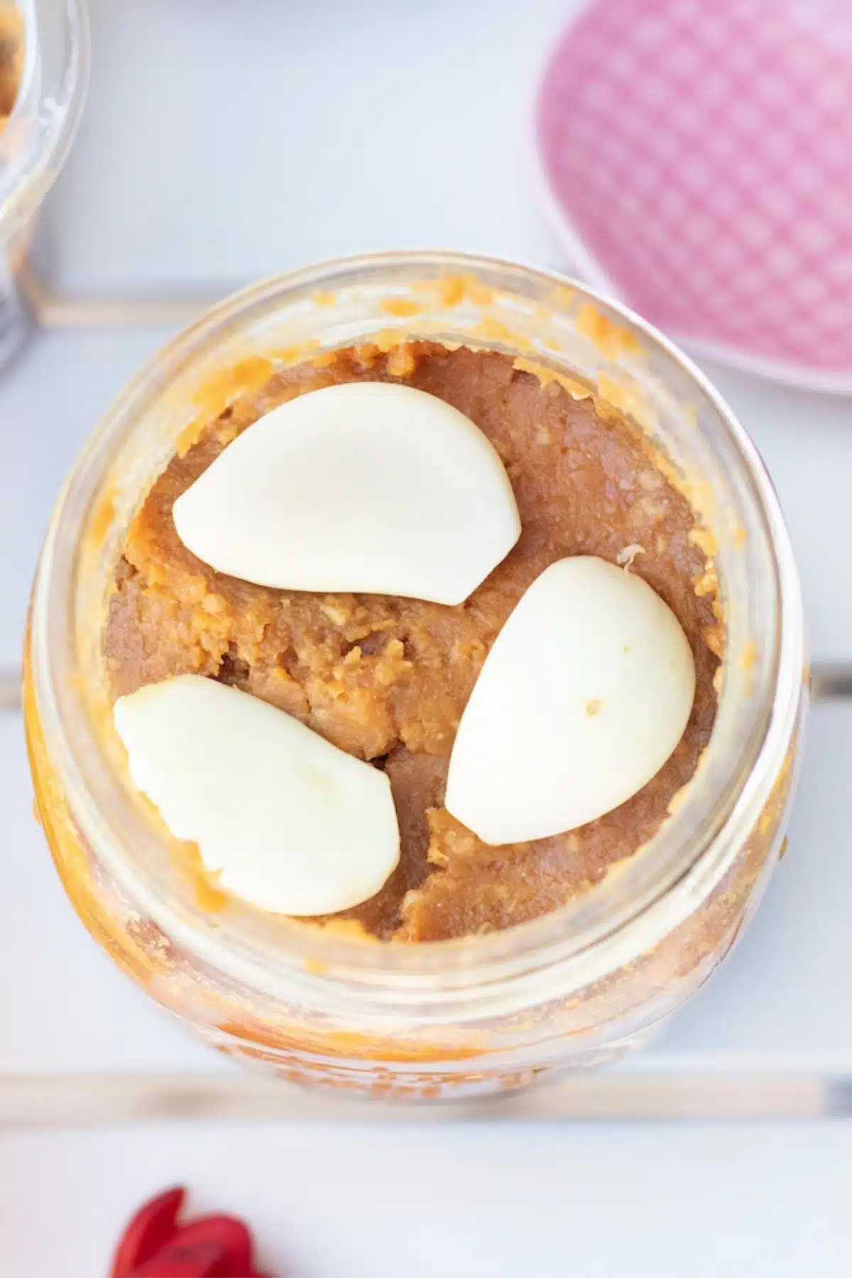 Looking down into a glass jar filled with white miso that has cloves of garlic embedded in layers.